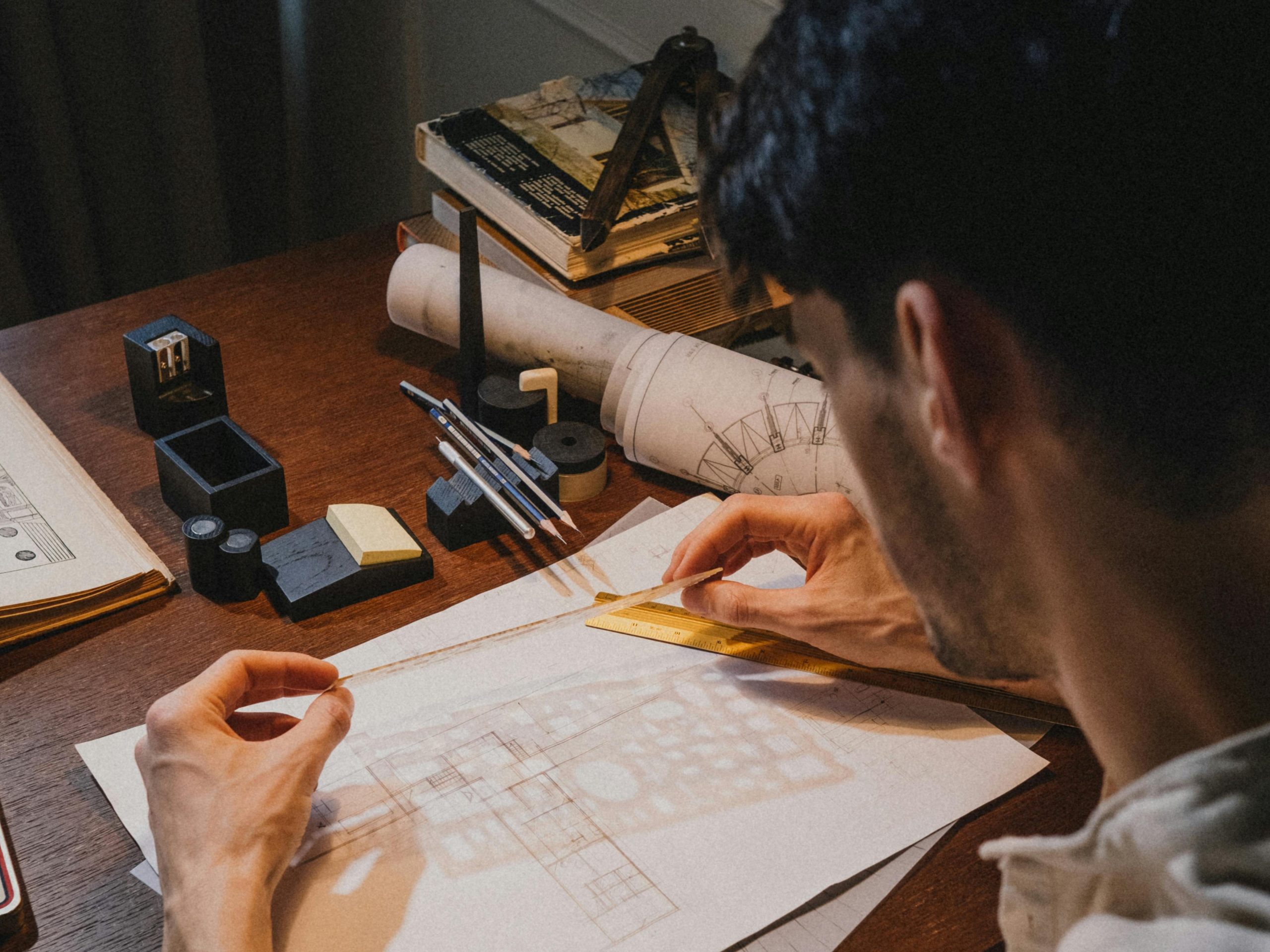 Accueil Man drawing architectural plans on a desk with various tools and blueprints.
